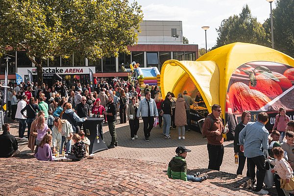 Das Foto zeigt eine große Gruppe von Menschen, darunter viele Kinder, bei strahlendem Sonnenschein bei der EDEKA Saisoneröffnung 2024 auf dem Platz vor der tectake ARENA: