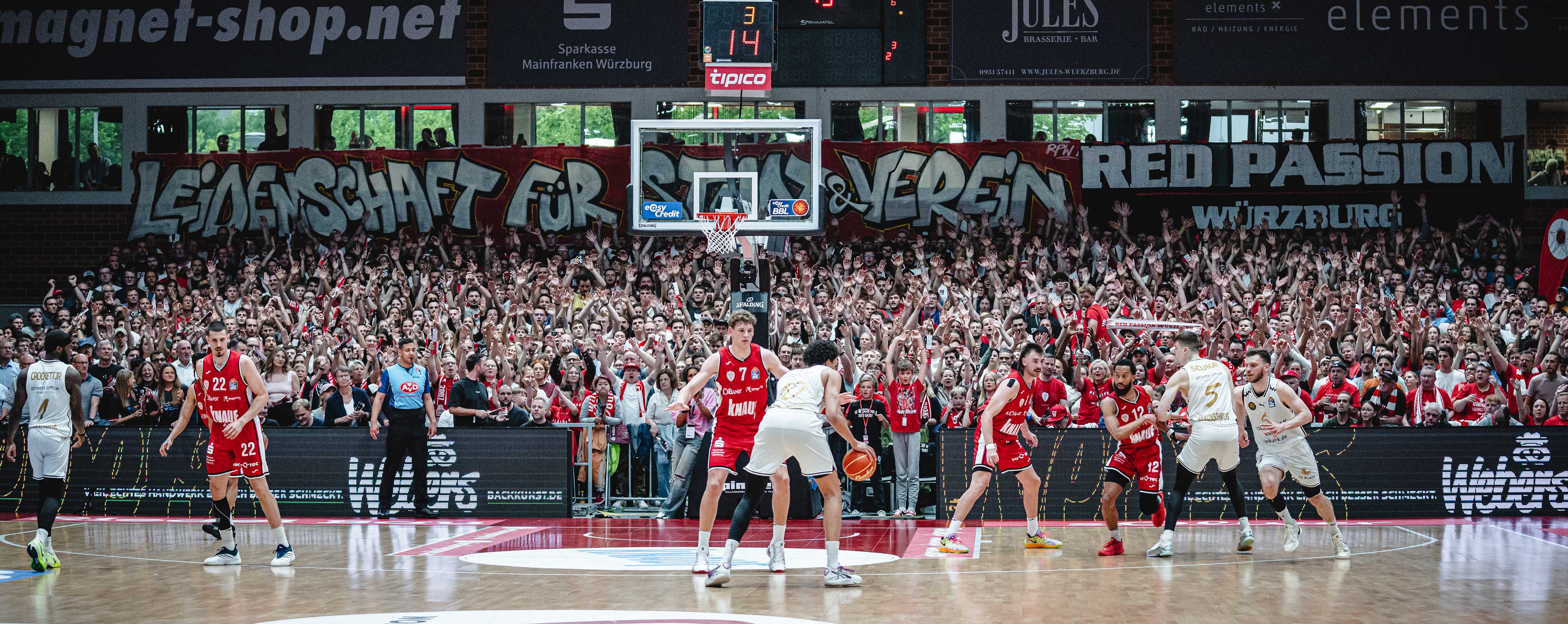 Spielsituation vor dem Korb der Würzburger mit Fans im Hintergrund